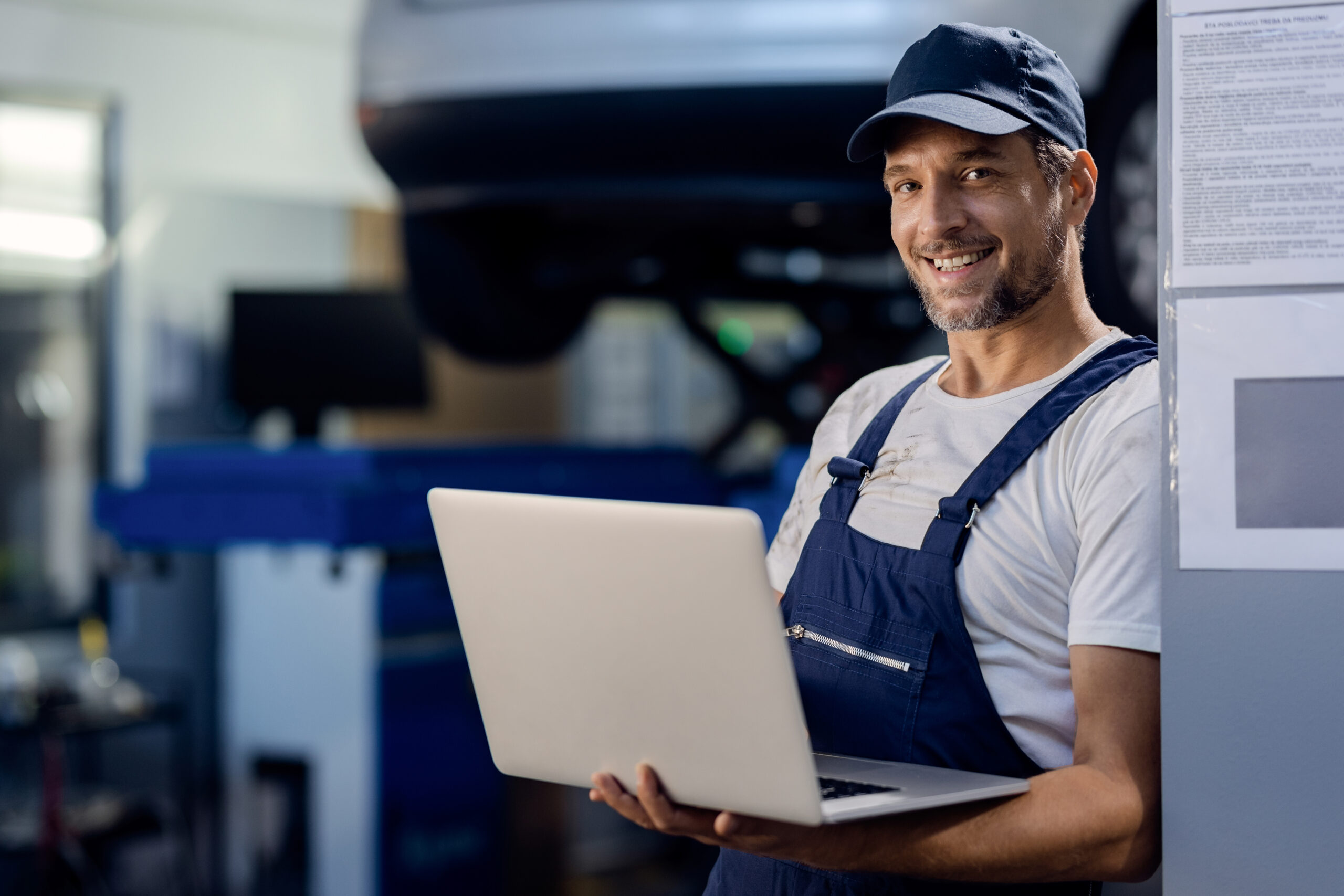 NEXT CLOUD happy mechanic working on a computer at auto repair shop.