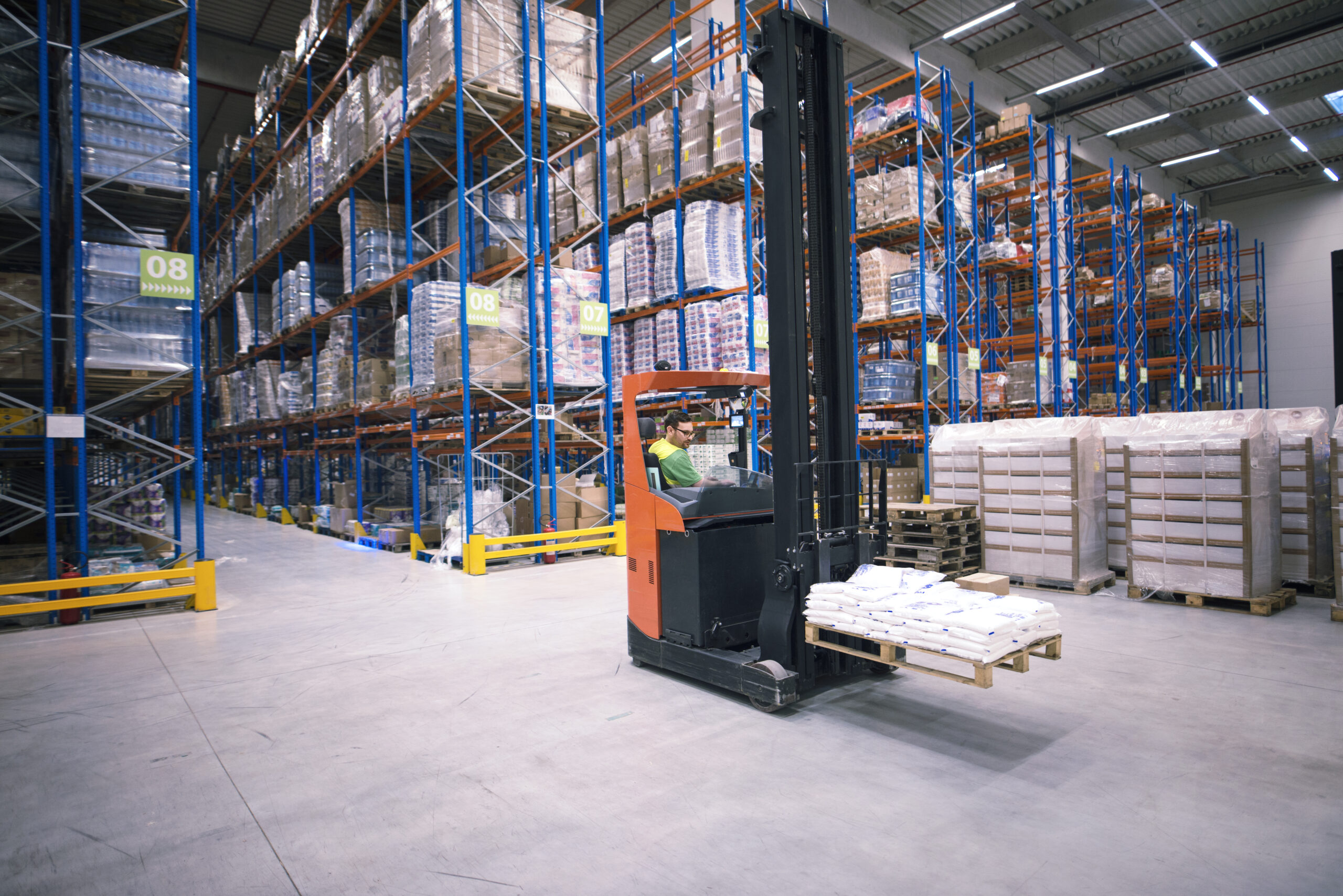 NEXT CLOUD worker operating forklift machine and relocating goods in large warehouse center.